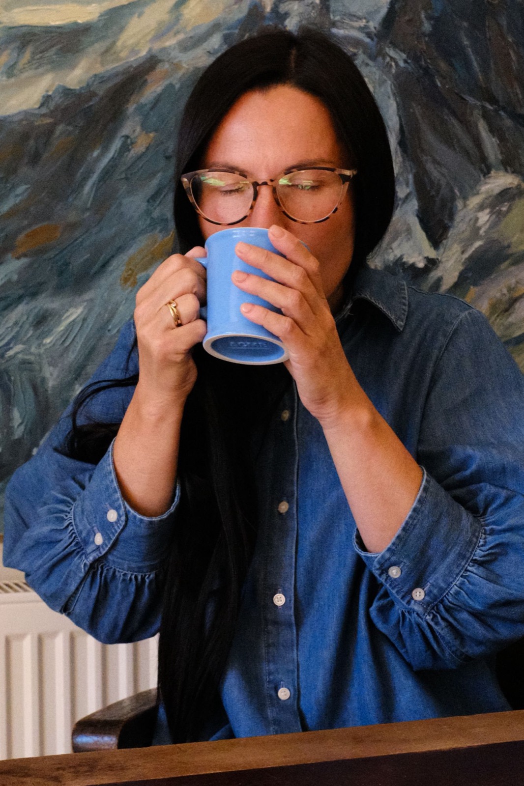Diana with eyes closed, sipping from a blue mug